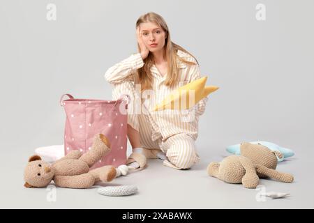 Müde junge Mutter, die Spielzeug in die Tasche auf grauem Hintergrund legt Stockfoto