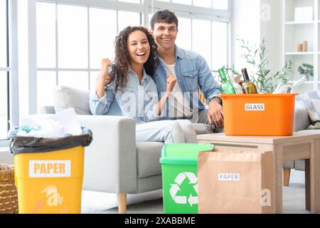 Glückliches junges Paar mit Müllcontainern, die zu Hause auf dem Sofa sitzen. Abfallsortierkonzept Stockfoto