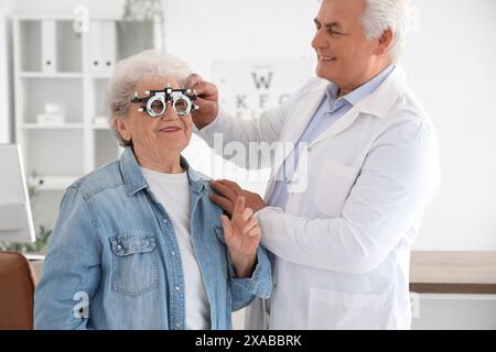 Männlicher Okulist, der einen Versuchsrahmen für Seniorinnen in der Klinik setzt Stockfoto