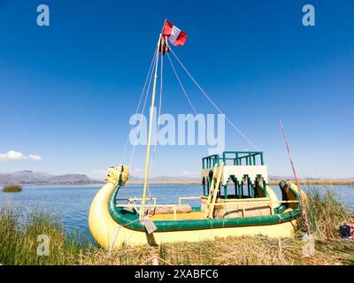 Lebendiges Schilfboot mit peruanischer Flagge, das auf dem ruhigen Wasser des titicacasees unter blauem Himmel schwimmt Stockfoto