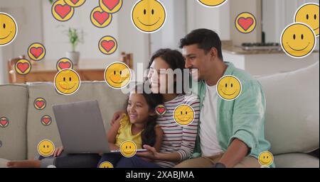 Bild von Emoji-Symbolen über glückliche birassische Familie mit Laptop Stockfoto