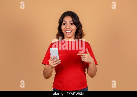 Lächelnde Frau, die das Smartphone hält und darauf zeigt Stockfoto