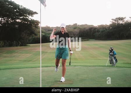 Eine Profi-Golferin in Rock und Kappe schlägt mit dem Ball ins Loch. Stockfoto