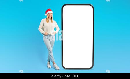 Frau Mit Weihnachtsmütze Posiert Mit Großem Smartphone-Mockup Stockfoto