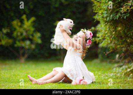 Kleines Mädchen Häschen im sonnigen Garten. Blühender Sommerpark. Kind hält Kaninchen bei Osterfeier. Eierjagd. Stockfoto