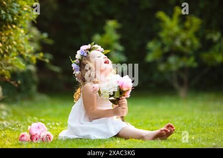 Kleines Mädchen mit Blumenstrauß im sonnigen Garten. Blühender Sommerpark. Kind mit Blumengeschenk für Geburtstagsfeier oder Osterfeier. Stockfoto