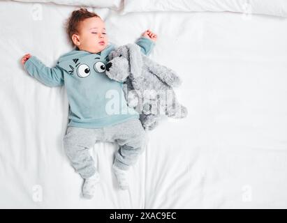 Entspannen Sie sich, ruhig und schlafend Baby mit Teddybär auf dem Bett in einem Haus mit Dachblick zum Ausruhen, Träumen oder Nickerchen. Kinderentwicklung, Spielzeug und schlafender Junge in A Stockfoto