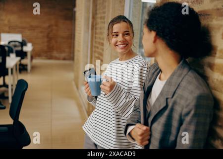 Lächelnde weibliche Angestellte sprechen und trinken in den Pausen in stilvollem Büro Kaffee Stockfoto