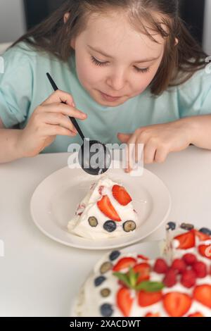 Das fröhliche kleine Mädchen isst Kuchen und steckt ihr ein großes Stück Dessert in den Mund. Ausgewählter Fokus. Hochwertige Fotos Stockfoto