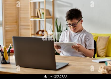 Entzückender Junge mit Down-Syndrom mit Brille, die zu Hause in Laptop-Aktivitäten eingetaucht ist. Stockfoto