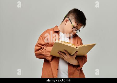 Ein kleiner Junge mit Down-Syndrom mit Brille liest ein Buch intensiv. Stockfoto