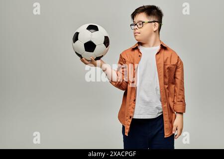 Kleines Kind mit Down-Syndrom mit einer Brille, die einen Fußball hält. Stockfoto