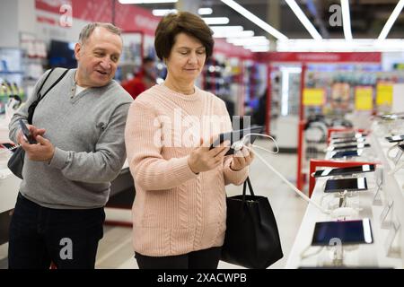 Seniorenpaar, das sich für Smartphone und Tablet im Tech-Store entscheidet Stockfoto