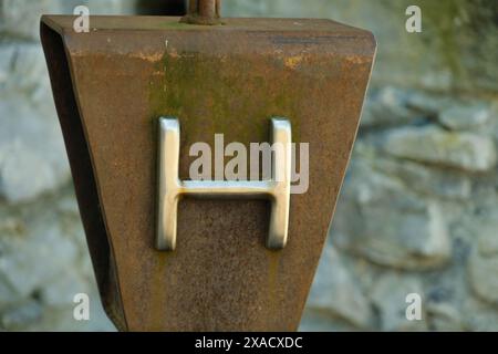 Ein rostiges Metallobjekt mit dem Buchstaben H drauf. Der Buchstabe H ist von einer grünen Moosfläche umgeben Stockfoto