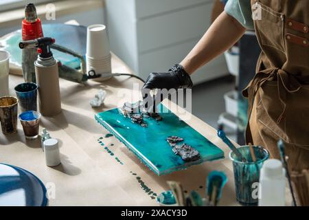 Handfläche der professionellen Frau, die Epoxidharzmalerei macht, in der Technik der flüssigen Flüssigkeitskunst arbeitet. Stockfoto