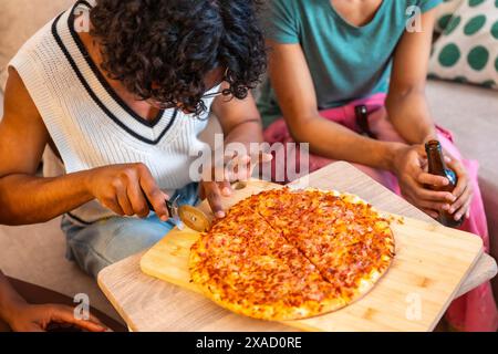 Nahaufnahme eines Mannes, der selbstgemachte Pizza schneidet, um sie mit Freunden zu Hause zu teilen Stockfoto