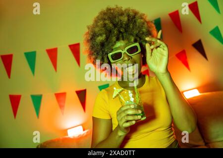 Coole afrikanerin mit Sonnenbrille, die Cocktails trinkt und zu Hause tanzt Stockfoto