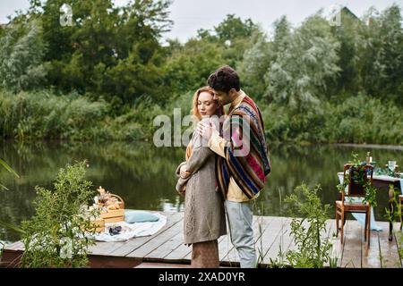 Ein Mann und eine Frau, gekleidet in Boho-Stil, umarmen sich liebevoll auf einem Dock in einem grünen Park zu einem romantischen Date. Stockfoto