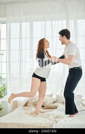 Ein Mann und eine Frau schlängeln und schweben anmutig, während sie auf einem Bett in einer gemütlichen Schlafzimmerumgebung tanzen. Stockfoto