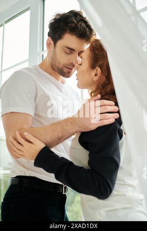 Ein Mann und eine Frau umarmen sich liebevoll vor einem Fenster, ihre Silhouetten umrandet vor dem sanften Licht. Stockfoto