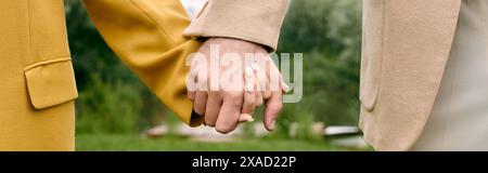 Eine Nahaufnahme von zwei Menschen, die Hände halten, ihre Finger in einer wunderschönen grünen Parklandschaft verflochten. Stockfoto