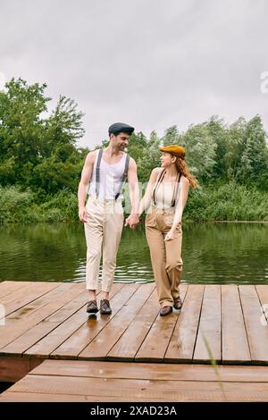 Ein Mann und eine Frau, lässig gekleidet, spazieren Hand in Hand über eine rustikale Holzbrücke in einer üppig grünen Parklandschaft. Stockfoto