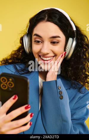 Eine junge Frau mit lockigem Haar, die Kopfhörer trägt und ein Handy ansieht, taucht in die Welt der Musik und Kommunikation ein. Stockfoto