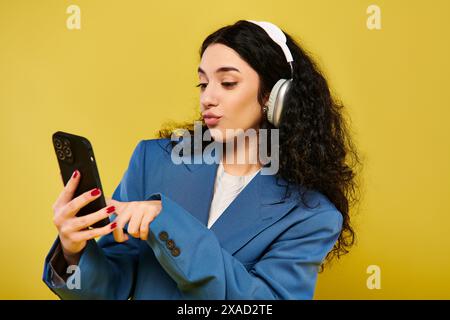 Eine junge, brünette Frau mit Kopfhörern blickt auf ihr Handy, eingetaucht in die Musik, die durch ihre Ohren spielt. Stockfoto