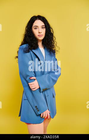 Eine stilvolle, junge Brünette mit lockigen Haaren posiert vor einem leuchtend gelben Hintergrund und strahlt Selbstvertrauen und Persönlichkeit aus. Stockfoto