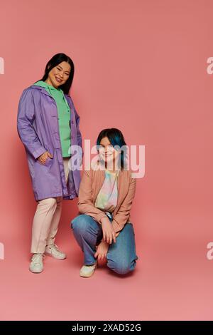 Asiatische Mutter und ihre Teenager-Tochter posieren selbstbewusst vor einem rosa Hintergrund in einem stilvollen Studio-Setting. Stockfoto