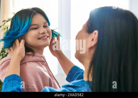 Eine asiatische Mutter mit blauen Haaren kämmt sanft die Haare ihrer Teenager-Tochter in einem zwanglosen Zuhause. Stockfoto