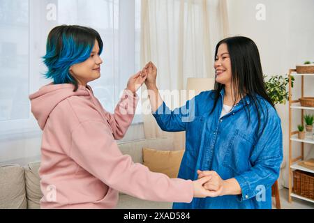 Eine asiatische Mutter und ihre Tochter im Teenageralter stehen beiläufig gekleidet nebeneinander in einem gemütlichen Wohnzimmer. Stockfoto