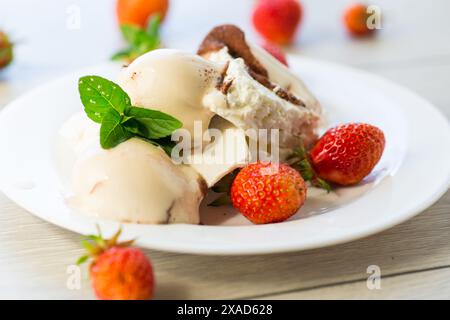 Frischer Bio-Hüttenkäse mit Erdbeeren und Eis auf einem Teller auf einem Holztisch. Stockfoto