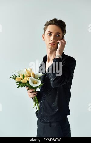 Eine junge queere Person ist Multitasking und spricht am Telefon, während sie in einem Studio einen Blumenstrauß hält. Stockfoto