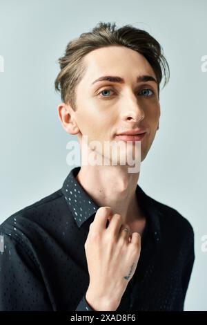 Ein junger Mann in einem schwarzen Hemd, der in einem Studio vor grauem Hintergrund posiert und Selbstvertrauen und Stolz ausstrahlt. Stockfoto