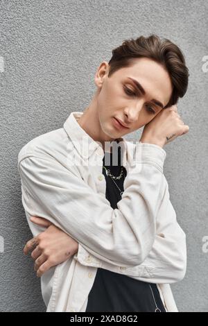 Ein junger Mann in stilvoller Kleidung lehnt sich an eine Wand und strahlt ein Gefühl von Rebellion und Besinnung aus. Stockfoto