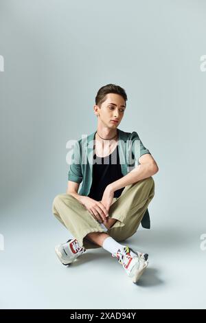 Eine junge queere Person sitzt auf dem Boden, trägt eine grüne Jacke und Turnschuhe und strahlt Vertrauen und Stolz in einem Studio aus. Stockfoto