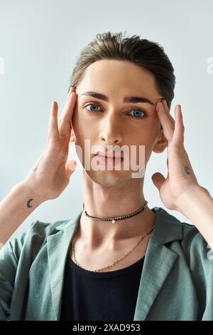 Eine junge queere Person, die mit Händen auf dem Kopf steht, tief besinnt, in einem Atelier mit grauem Hintergrund. Stockfoto