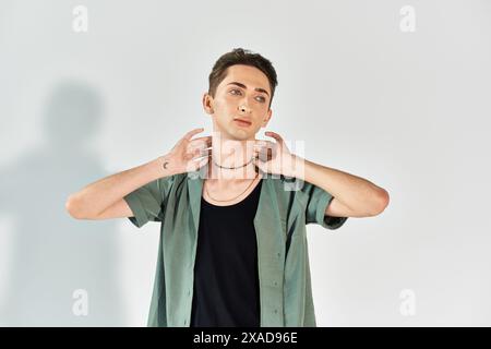 Eine junge queere Person posiert selbstbewusst in einem Studio mit einem grünen Hemd auf grauem Hintergrund. Stockfoto