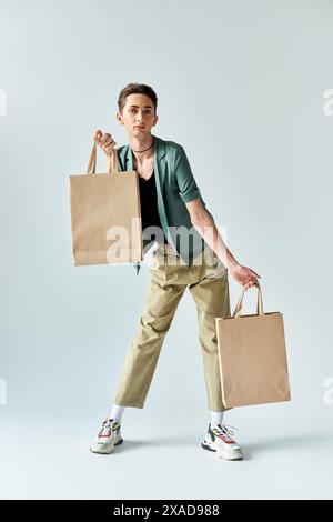 Eine junge queere Person hält stolz Einkaufstaschen vor weißem Hintergrund. Stockfoto