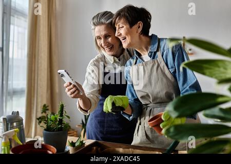 Zwei Frauen in Schürzen, die einen Moment auf ihrem Handy festhalten. Stockfoto