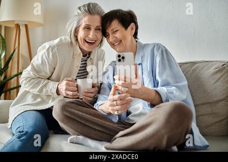 Zwei ältere Frauen sitzen auf einer Couch und machen glücklich ein Selfie zusammen. Stockfoto