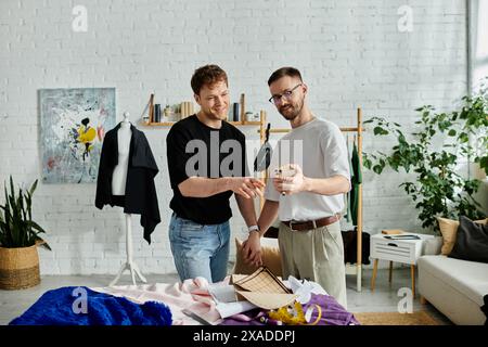 Zwei Designer arbeiten an einem digitalen Gerät zusammen und tauschen in einer Designerwerkstatt Ideen für trendige Kleidung aus. Stockfoto