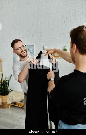 Zwei Männer arbeiten in einer Designerwerkstatt zusammen, einer hält ein schwarzes Hemd, der andere passt es an. Stockfoto