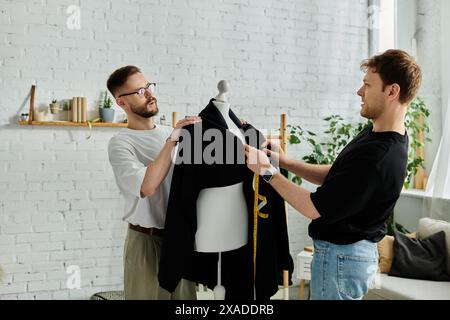 Zwei Männer, Designer, stehen vereint in einer kreativen Werkstatt und arbeiten gemeinsam an trendigen Kleidern. Stockfoto