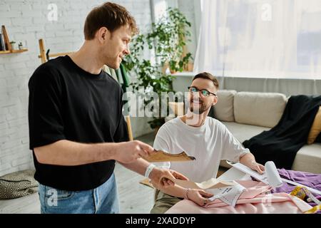 Zwei Männer, beide Designer, arbeiten in ihrer Werkstatt an trendigen Kleidern zusammen. Stockfoto