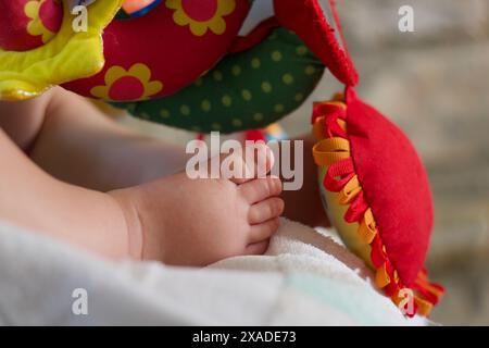 Details zum Baby-Jungen-Fuß, der in der Nähe von bunten Spielzeugen schläft, Kopierraum Stockfoto