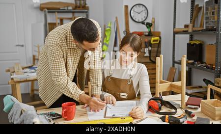 Ein Mann und eine Frau in einer Werkstatt arbeiten an einem Dokument zusammen, umgeben von Holzwerkzeugen und -Materialien. Stockfoto