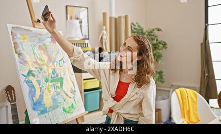 Selbstbewusster junger Künstler macht fröhliches Selfie während der Malerei im Kunststudio Stockfoto