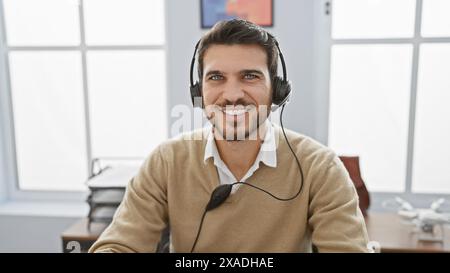 Lächelnder hispanischer Mann mit Headset in einem hellen Büro, der Professionalität und freundlichen Kundenservice vermittelt. Stockfoto